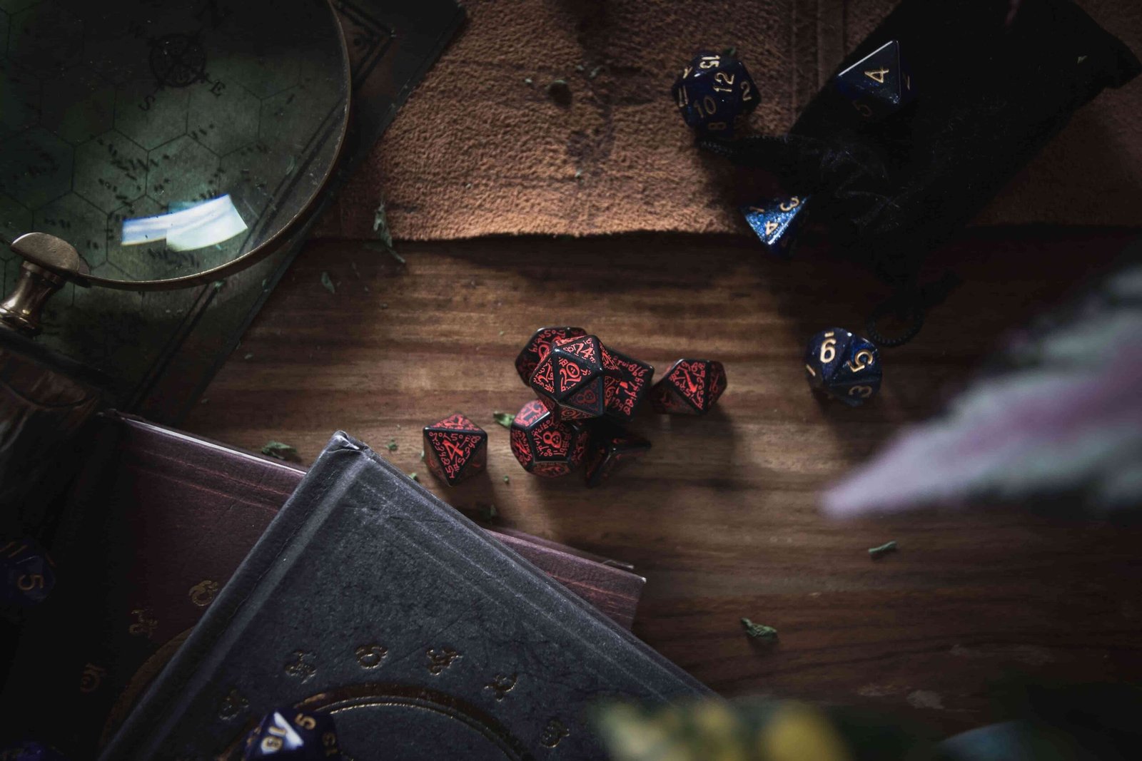 Black and red polyhedral dice scattered on a dark wooden table beside old hardback books