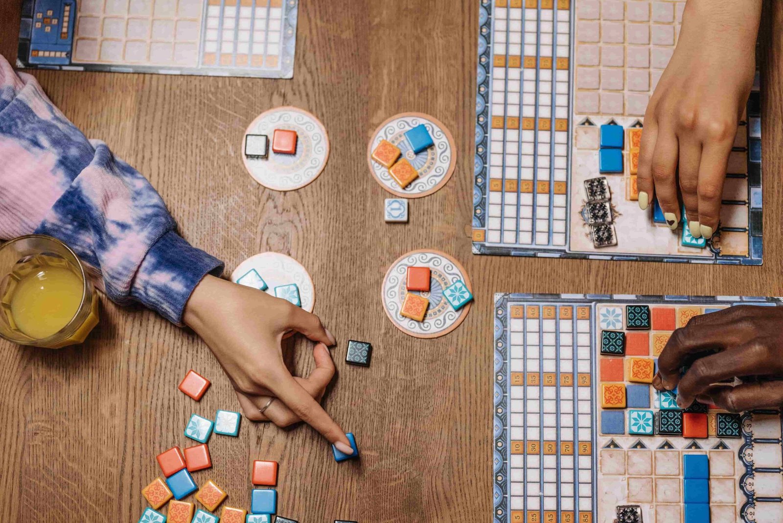 Overhead view of two people placing coloured tiles onto their player boards during a tabletop game